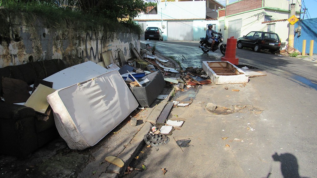 Moradores da Rua Geneuna, no Jardim Carioca, colocam lixo e entulho para tampar buracos e segurar vazamento de esgoto que há semanas corre no local